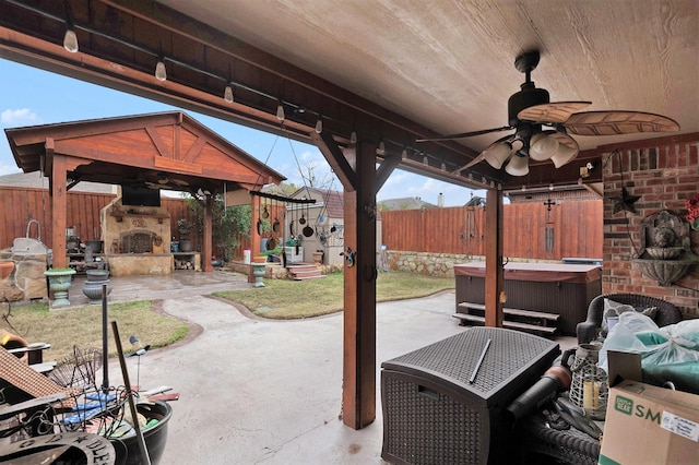 view of patio / terrace featuring ceiling fan, a gazebo, a hot tub, and an outdoor stone fireplace