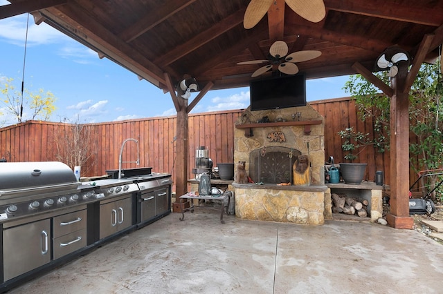 view of patio featuring an outdoor kitchen, ceiling fan, a grill, and an outdoor stone fireplace