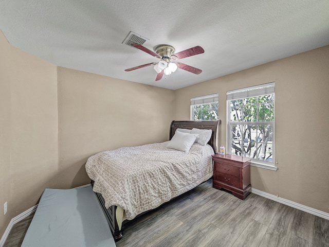 bedroom with a textured ceiling, light hardwood / wood-style flooring, and ceiling fan