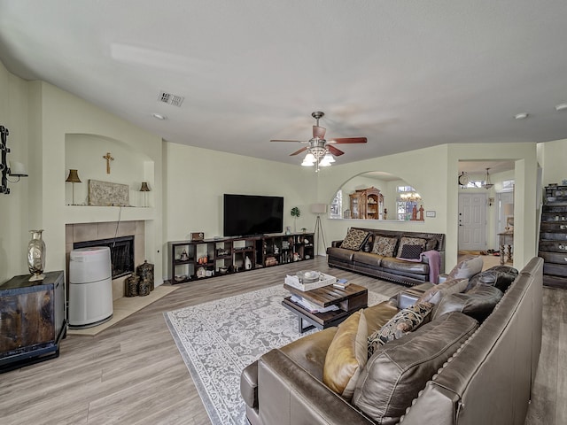 living room with a tile fireplace, light wood-type flooring, and ceiling fan with notable chandelier