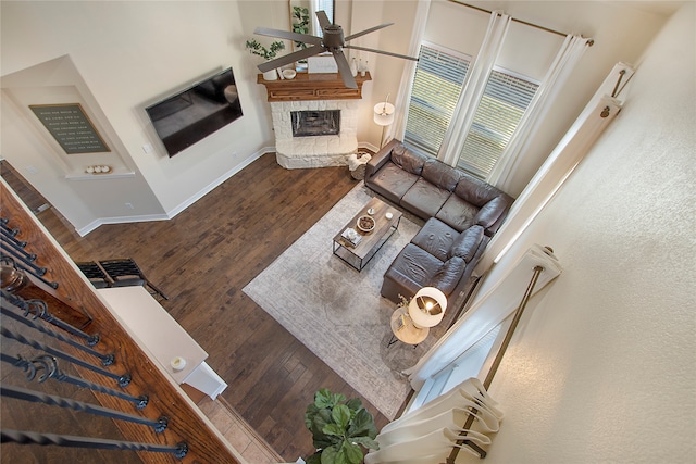 living room with wood-type flooring, a stone fireplace, and ceiling fan