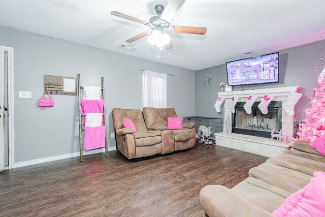 living room with a stone fireplace, ceiling fan, and dark wood-type flooring