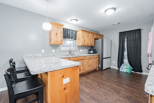 kitchen featuring dark wood-type flooring, hanging light fixtures, sink, kitchen peninsula, and stainless steel refrigerator