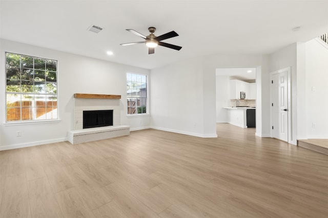 unfurnished living room featuring ceiling fan, light wood-type flooring, and a brick fireplace