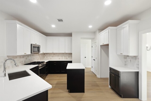 kitchen with appliances with stainless steel finishes, backsplash, sink, light hardwood / wood-style floors, and a kitchen island