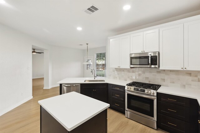 kitchen featuring sink, stainless steel appliances, light hardwood / wood-style floors, decorative light fixtures, and a kitchen island