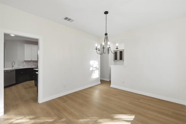 unfurnished dining area with light hardwood / wood-style flooring, a chandelier, and sink