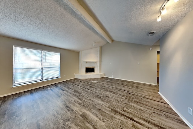 unfurnished living room with wood-type flooring, vaulted ceiling with beams, a textured ceiling, and a brick fireplace