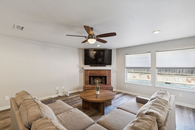 living room with a brick fireplace, ceiling fan, a textured ceiling, and hardwood / wood-style flooring