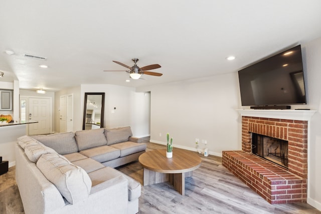 living room with hardwood / wood-style floors, a brick fireplace, and ceiling fan