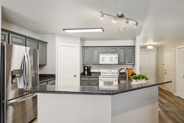 kitchen with white appliances, gray cabinets, dark stone countertops, dark hardwood / wood-style floors, and an island with sink