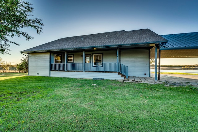 back house at dusk featuring a lawn and a porch