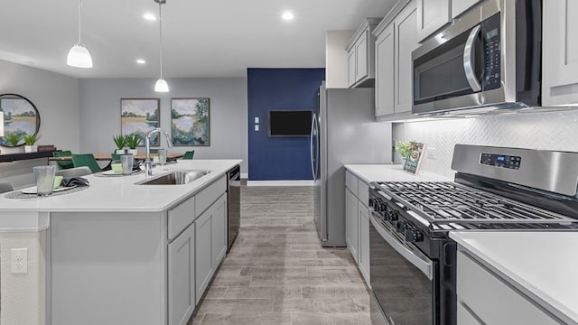 kitchen featuring gray cabinetry, sink, stainless steel appliances, an island with sink, and decorative light fixtures