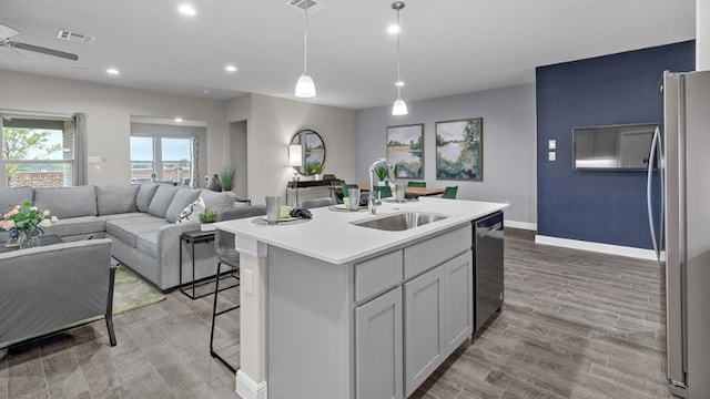 kitchen with sink, stainless steel appliances, light hardwood / wood-style flooring, decorative light fixtures, and a kitchen island with sink