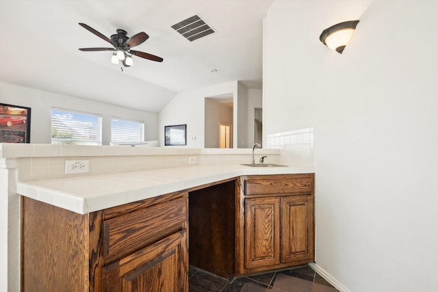 kitchen with kitchen peninsula, ceiling fan, sink, tile countertops, and lofted ceiling