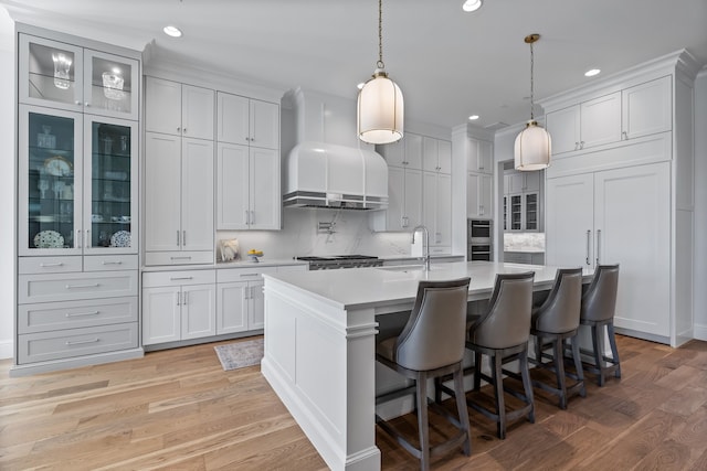 kitchen featuring a center island with sink, decorative backsplash, pendant lighting, and light hardwood / wood-style flooring