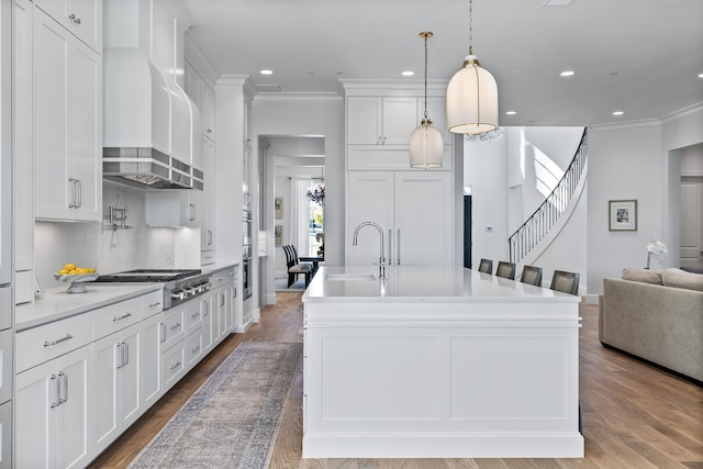 kitchen with wall chimney exhaust hood, sink, pendant lighting, light hardwood / wood-style floors, and white cabinetry