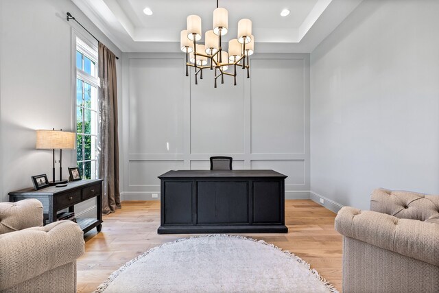 office area with light hardwood / wood-style floors, a raised ceiling, and an inviting chandelier