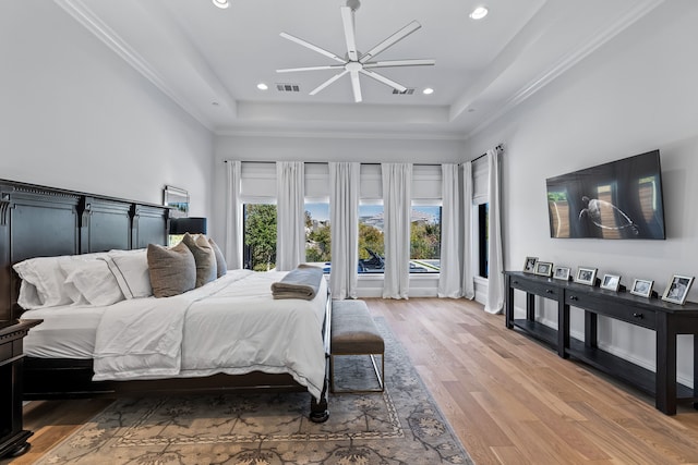 bedroom with hardwood / wood-style flooring, ceiling fan, a raised ceiling, and crown molding