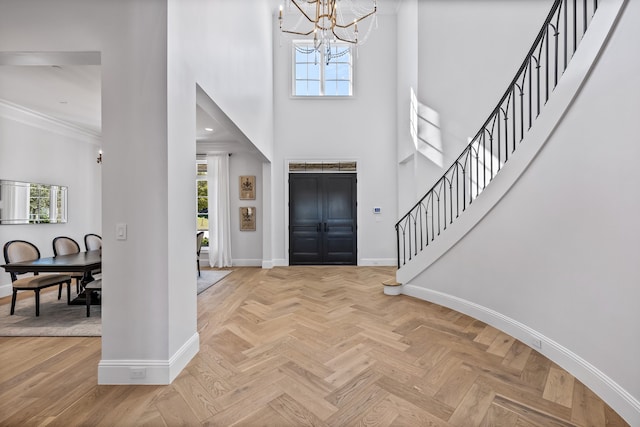 foyer entrance featuring a chandelier, crown molding, a high ceiling, and light parquet floors