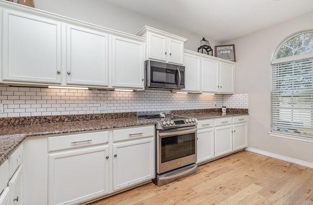 kitchen featuring appliances with stainless steel finishes, white cabinetry, dark stone countertops, tasteful backsplash, and light wood-type flooring