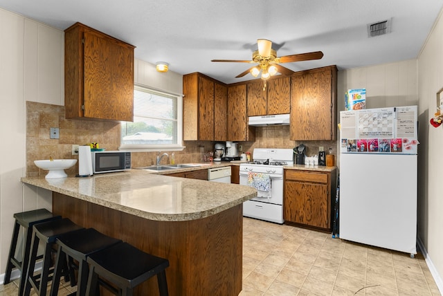 kitchen with kitchen peninsula, white appliances, tasteful backsplash, and sink