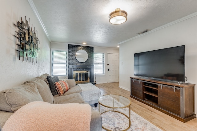 living room with a brick fireplace, ornamental molding, a textured ceiling, and light wood-type flooring