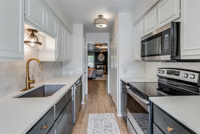 kitchen with sink, light hardwood / wood-style flooring, a fireplace, appliances with stainless steel finishes, and white cabinetry