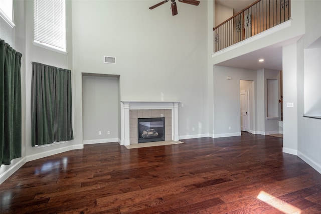 unfurnished living room featuring a fireplace, a towering ceiling, dark hardwood / wood-style floors, and ceiling fan