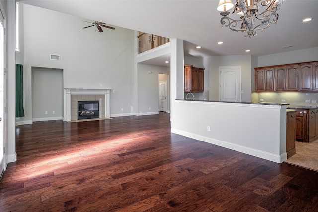 kitchen with backsplash, ceiling fan with notable chandelier, a towering ceiling, a fireplace, and dark hardwood / wood-style flooring