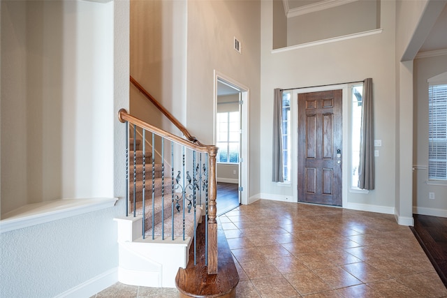 foyer entrance with crown molding, tile patterned flooring, and a towering ceiling