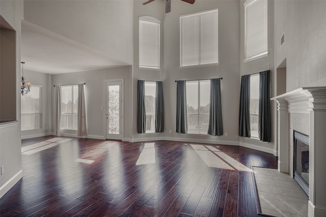 unfurnished living room featuring a tiled fireplace, hardwood / wood-style floors, a towering ceiling, and ceiling fan with notable chandelier