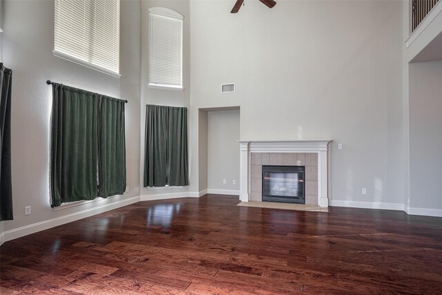 unfurnished living room featuring a fireplace, ceiling fan, dark hardwood / wood-style flooring, and a high ceiling