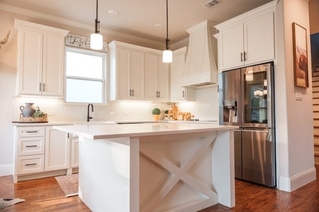 kitchen featuring custom exhaust hood, stainless steel fridge with ice dispenser, white cabinetry, decorative light fixtures, and a kitchen island