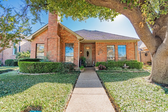 view of front facade featuring a shingled roof, a front yard, brick siding, and a chimney