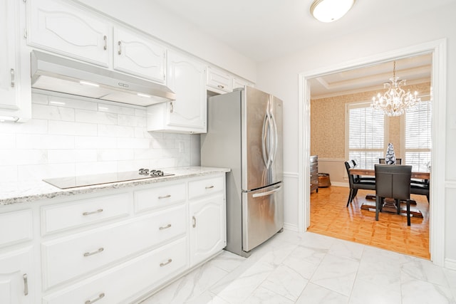 kitchen featuring marble finish floor, black electric cooktop, freestanding refrigerator, and under cabinet range hood