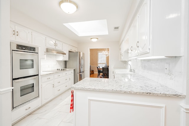 kitchen featuring visible vents, a peninsula, stainless steel appliances, under cabinet range hood, and a sink