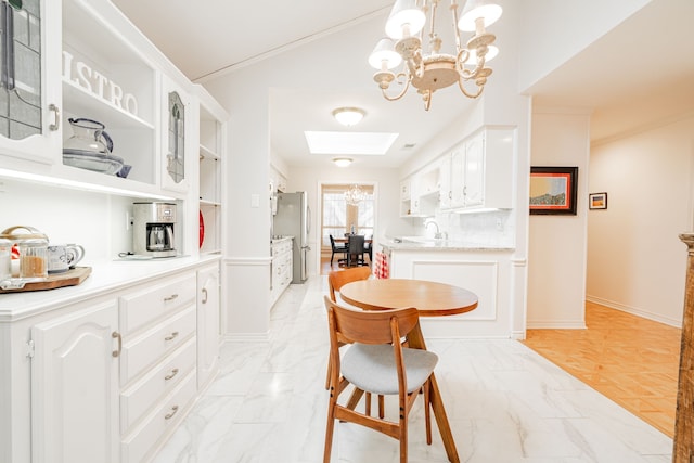 kitchen featuring a skylight, marble finish floor, glass insert cabinets, freestanding refrigerator, and white cabinetry