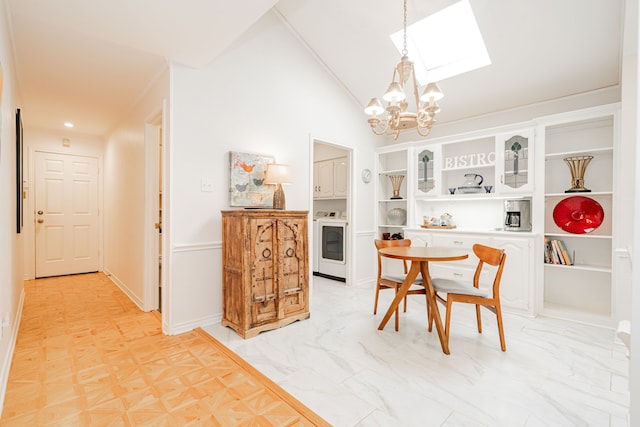 dining space featuring lofted ceiling with skylight, washer / clothes dryer, a notable chandelier, and marble finish floor