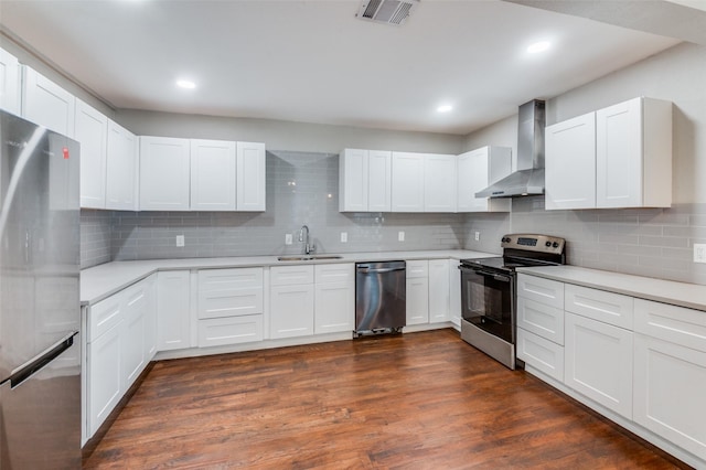 kitchen with appliances with stainless steel finishes, light countertops, wall chimney range hood, white cabinetry, and a sink