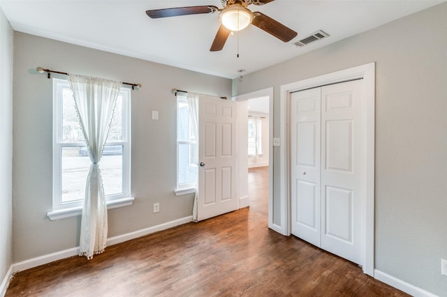 unfurnished bedroom featuring baseboards, multiple windows, visible vents, and dark wood-type flooring