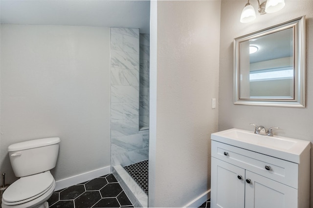 bathroom featuring toilet, vanity, baseboards, a tile shower, and tile patterned floors