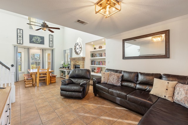 living room featuring a textured ceiling, crown molding, light tile patterned floors, built in features, and a stone fireplace