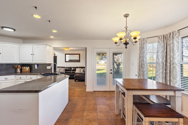 kitchen featuring french doors, white cabinets, sink, tasteful backsplash, and decorative light fixtures