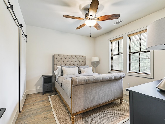 bedroom with ceiling fan, a barn door, and dark wood-type flooring