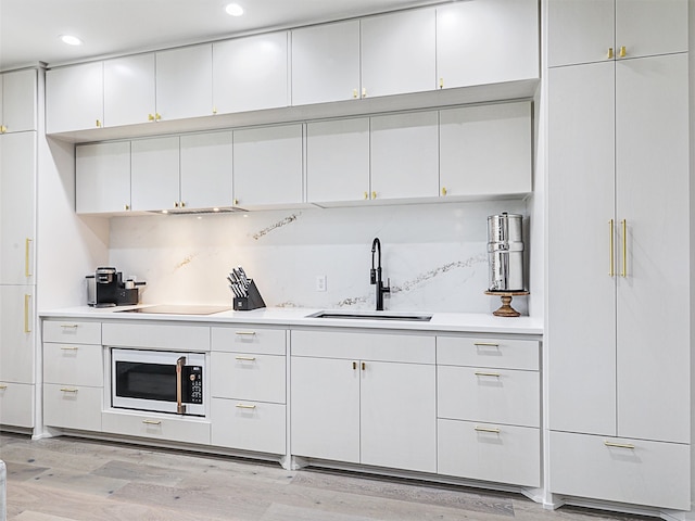 bar featuring sink, backsplash, light wood-type flooring, white cabinets, and appliances with stainless steel finishes