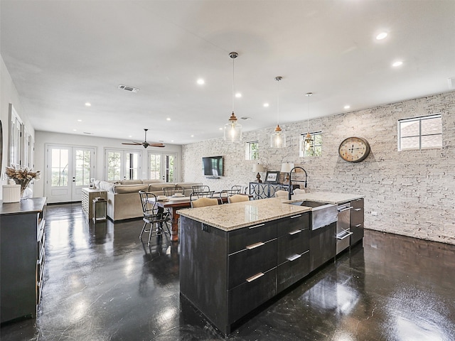 kitchen featuring light stone countertops, french doors, sink, hanging light fixtures, and a center island with sink