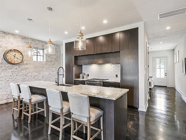 kitchen with high end range, sink, hanging light fixtures, decorative backsplash, and an island with sink