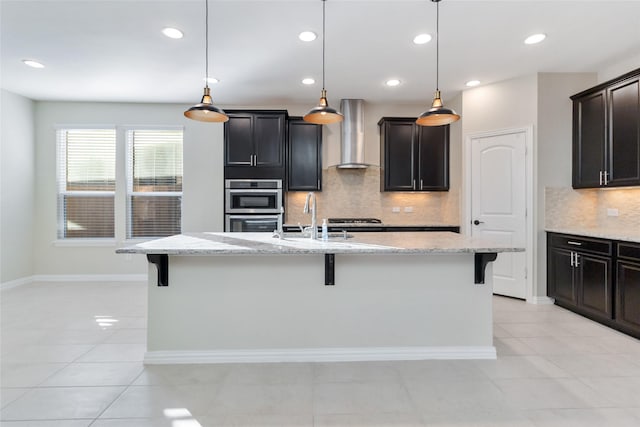 kitchen with a kitchen bar, wall chimney range hood, and an island with sink