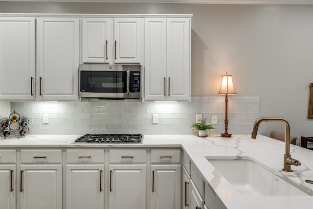 kitchen featuring tasteful backsplash, light stone counters, stainless steel appliances, sink, and white cabinets